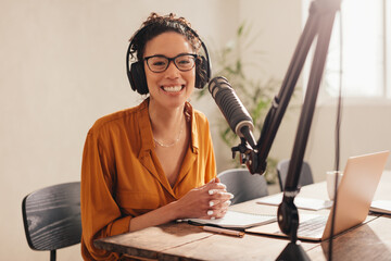 Cheerful woman recording a podcast from home - obrazy, fototapety, plakaty