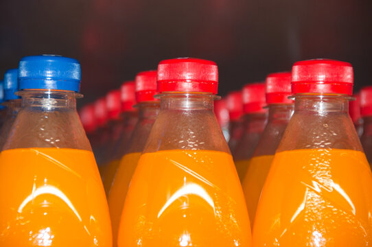 Close up of plasric bottles in shelf with orange liquid inside.