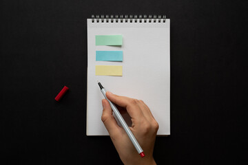 Taking notes in blank paper white notebook colorful post-it woman hand and red pencil on wooden table background. new year's resolution, goals. 2021. coronavirus. home office, to do list, copy space. 