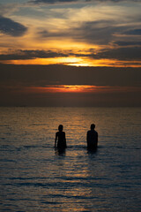Naklejka na ściany i meble Silhouette couple standing midth of sea in the warm light evening time
