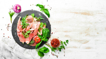 Prosciutto with arugula and basil on a black plate. Spanish cuisine. Top view. Free space for your...