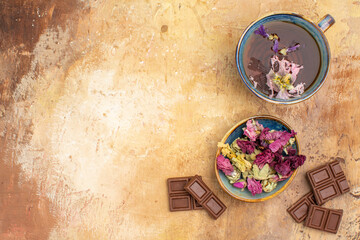 Fototapeta na wymiar A cup of hot herbal tea flowers and chocolate bars on mixed color bckground