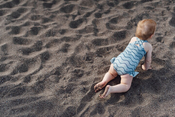 little child crawls and plays on the sandy beach. Family vacation at the sea.