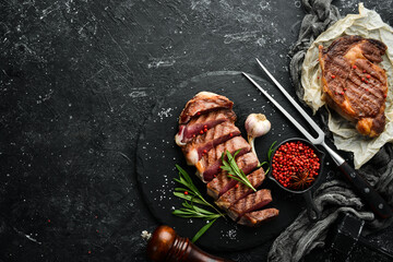 Grilled sliced beef steak with rosemary and spices on a black stone background. Top view. Free...