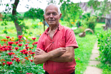retired man posing next to a flower bed on a personal plot in a village in summer