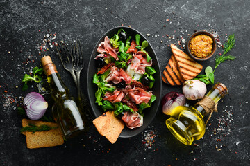 Fototapeta na wymiar Prosciutto salad with olives in a black bowl. Spanish cuisine. Top view. Free space for your text. Rustic style.