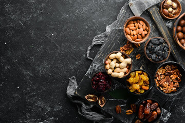 Obraz na płótnie Canvas Set of nuts and dried fruits and berries on a black stone background. Top view. Free space for your text.