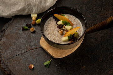 Oatmeal cooked in milk with fruits, nuts and dried fruits. Delicious and healthy breakfast served in a deep ceramic bowl.