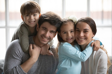 Head shot portrait smiling parents with two adorable little kids, happy father piggy backing...