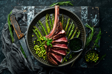 Tomahawk steak on the bone. Grilled steak with asparagus and green peas. On a black background. Top...