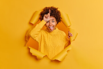 Playful crazy young woman makes looser gesture over forehead sticks out tongue says someone you are...