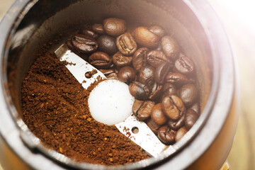 Electric coffee-mill machine with roasted coffee beans on the kitchen table with green tabletop