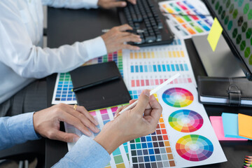 Graphic designer or creative working together coloring using graphics tablet and a stylus at desk with colleague.