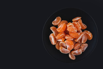 Tangerine slices on a black plate on a black background