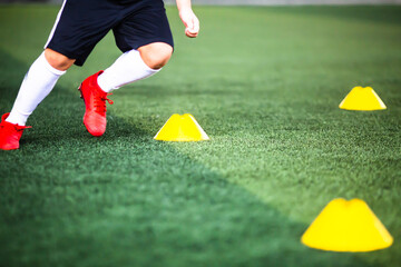 Selective focus to cone marker with blurry boy soccer player is jogging on green artificial turf.