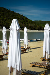 Wooden sun loungers and beach umbrellas on a sandy lakeshore in Sukko, Russia on a hot summer day