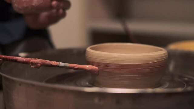 The process of making tableware from natural clay on a potter's machine, the hand paints the bowl with a brush with clay paint   