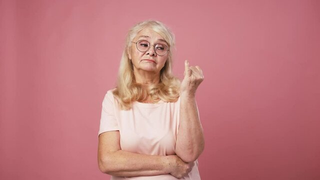 Senior lady in glasses deciding solution, counting on fingers from one to five, pink studio background