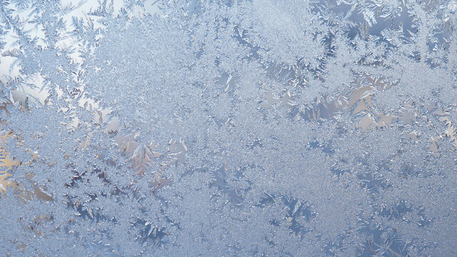 Ice and frost on the window glass in winter. A pattern of frozen water crystals, similar to the leaves of fantastic plants or jewels. Light blue backdrop. Abstract natural background or wallpaper