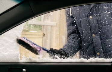 Male driver with gloves brushes snow off passenger side window of car - view from passenger compartment