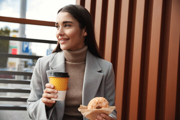 Businesswoman having lunch in outdoor cafe. Young woman eating donut and drinking coffee on street, stop in restaurant for a break