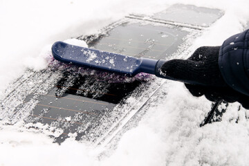 Gloved male driver sweeps snow off car rear window with special brush