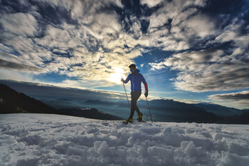 Naklejka na ściany i meble Athlete man trains with snowshoes at sunset in the mountains