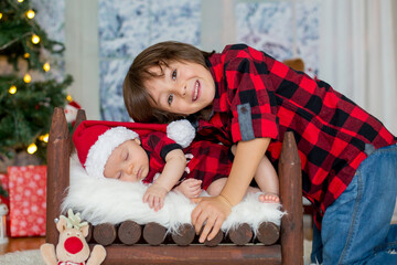 Portrait of newborn baby and his brother in Santa clothes, sleeping in little baby bed