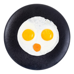 top view of fried eggs and slice of carrot on black plate isolated on white background. Fried eggs like face with open mouth