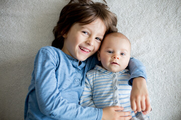 Happy brothers, baby and preschool children, hugging at home on white blanket