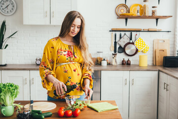 Pregnant girl preparing vegetable salad in the kitchen