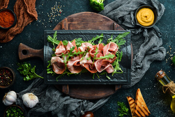 Jamon and arugula on a black stone plate. Prosciutto. Top view. Free space for text.
