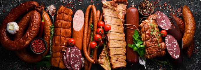 Set of sausage, salami and smoked meat with rosemary and spices on a black stone background. Top...
