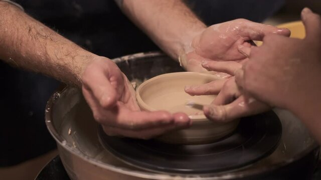 The process of preparing tableware from natural clay on a potter's machine, four hands  