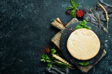 Pizza base on a black stone plate with basil. Top view. Rustic style.