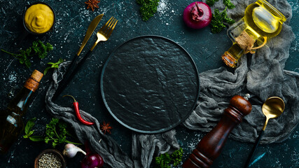 Kitchen banner: Spices, vegetables and cutlery on a black stone background. Top view. Free space...