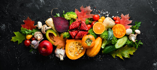 Autumn vegetables and fruits on a black stone background: Pumpkin, tomatoes, corn, pomegranate, persimmon, apple. Top view. Free copy space.