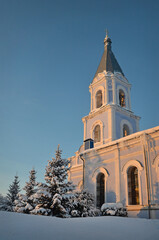 Bell tower of the orthodox church. Winter sunset. Pine trees in the snow. Beautiful russian winter.