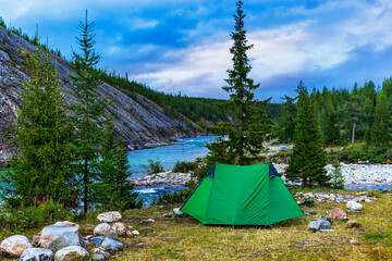 tent in a clearing among fir trees on the river bank