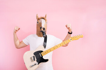 Man with horse mask showing the strength of his arms and with hanging electric guitar