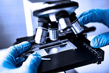 doctor wearing protective gloves using microscope researching corona virus microscopic cells...