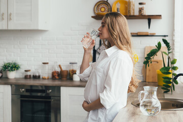 Pregnant girl drinking clean water in the kitchen