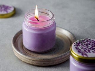 Aroma Candle. Lavender candle on a gray background. A match is set on fire with an aroma candle. Spring fragrance. Aromatherapy. Green in the background. Purple candle. Space for text. Spa.