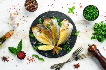 Smoked sea fish Vomer with parsley on a black stone plate. Top view. Free space for your text.