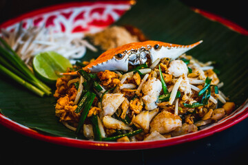a plate of fried Phad Thai noodles with crab meat, bean sprouts, scallions and raw scallions and a lime wedge on the side