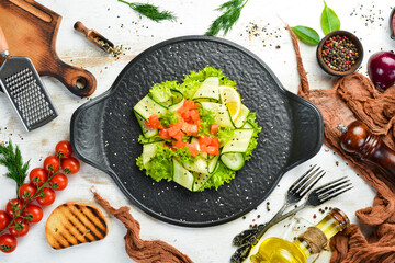 Salad with cucumber, salmon and lettuce. Healthy food. On a black stone plate. Top view.