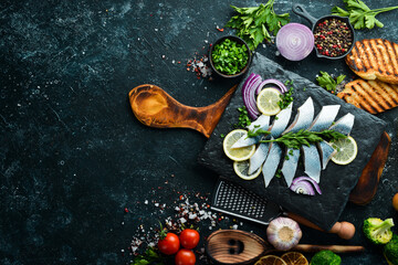 Salted herring with onion and lemon on a black stone board. Top view. Free space for your text.