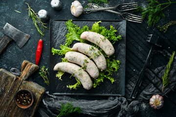Raw sausages with thyme and spices on a black stone plate. Top view. On a black background.