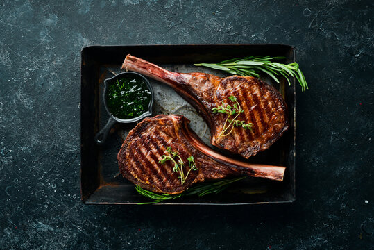 Juicy steak grilled on the bone with spices and herbs. On a black stone background. Top view. Free copy space.
