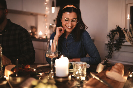 Smiling young woman enjoying a candlelit dinner party with frien